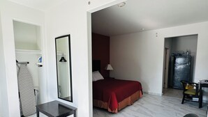 A hotel room with a bed, a desk, a chair, a mirror, and a wardrobe. - Lux Inn and Suites (Three Rivers)