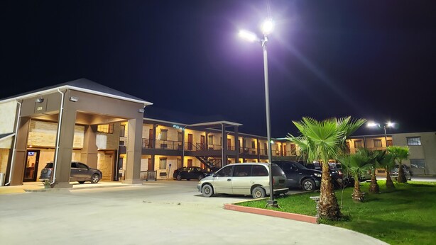 A multi-story hotel with a parking area, illuminated by street lamps. - Lux Inn and Suites (Three Rivers)