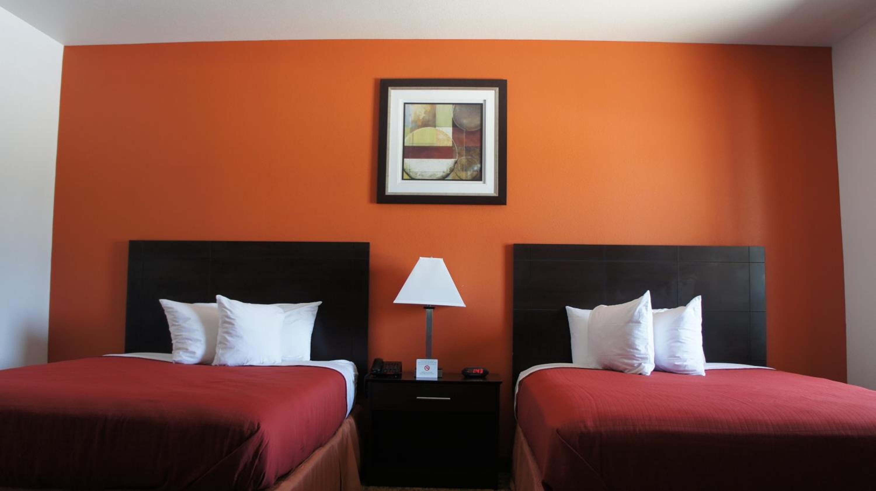 Habitación de hotel con dos camas, una mesita de noche, una lámpara y una obra de arte enmarcada en la pared.
