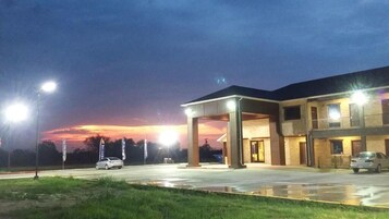A hotel with a covered parking area, multiple rooms, and a view of the sunset.