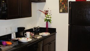 A kitchen with dark wooden cabinets, a black refrigerator, a coffee maker, and a vase with flowers. - Lux Inn and Suites (Three Rivers)