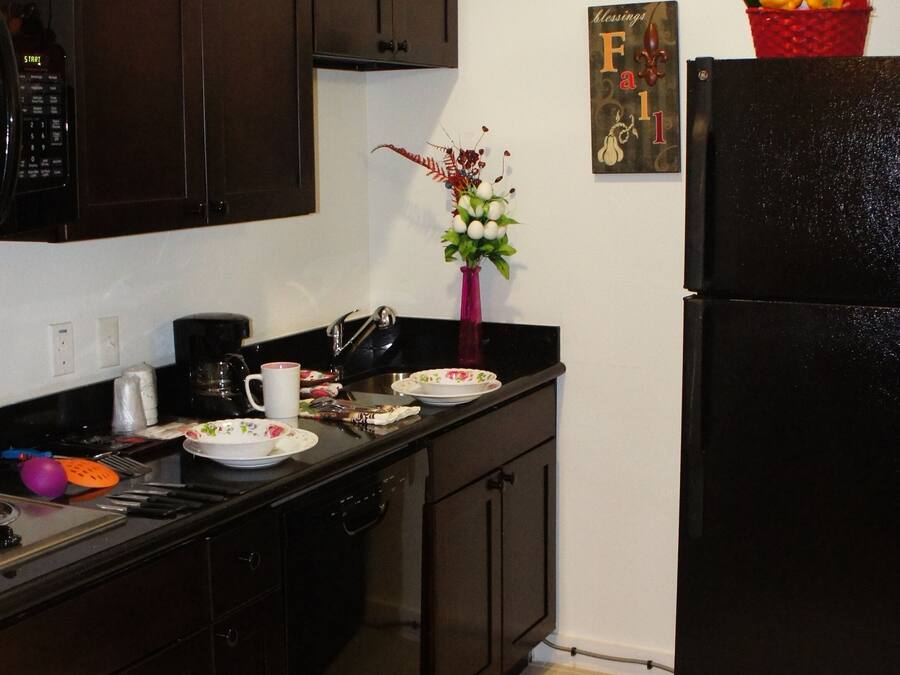 A kitchen with dark wooden cabinets, a black refrigerator, a coffee maker, and a vase with flowers.