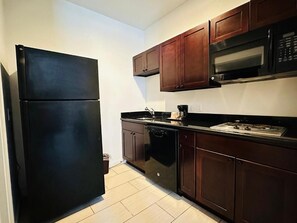 A kitchen with a black refrigerator, wooden cabinets, a microwave, and a dishwasher.