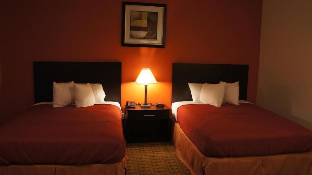Habitación de hotel con dos camas, una mesita de noche con lámpara y un cuadro en la pared.