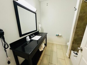 A bathroom with a black vanity, a mirror, a sink, a towel rack, and a shower area.