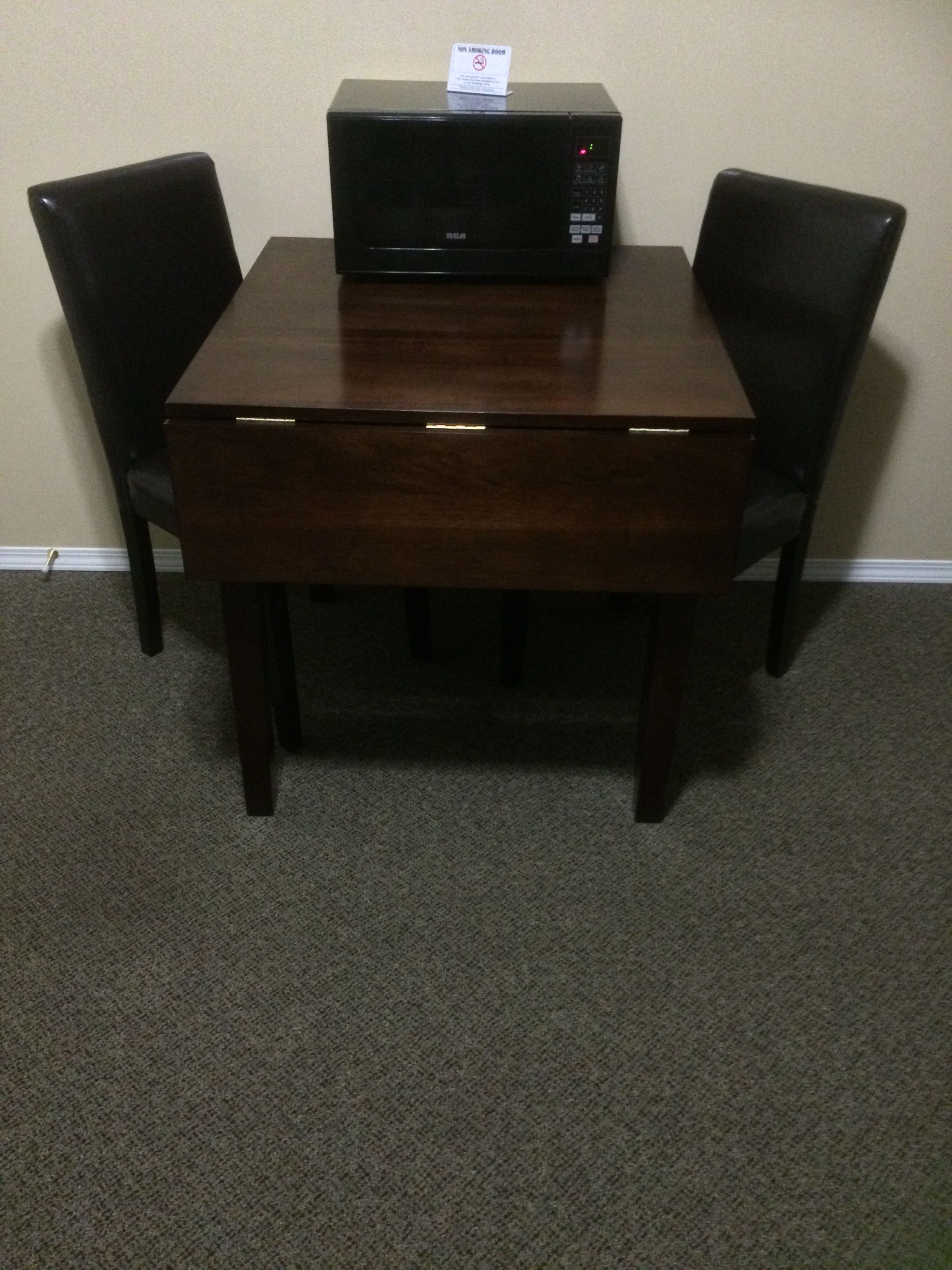 A dining table with a microwave on top, surrounded by four chairs.