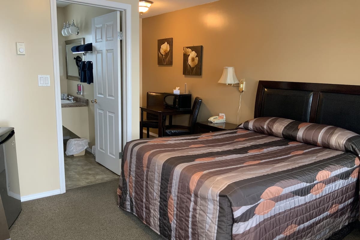 A hotel room with a bed, a desk, a chair, a lamp, and a bathroom visible through an open door.