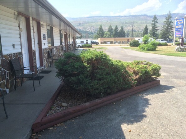 A motel with a covered porch, outdoor seating, and a view of mountains in the background. - Monte Carlo Motel (Barriere)