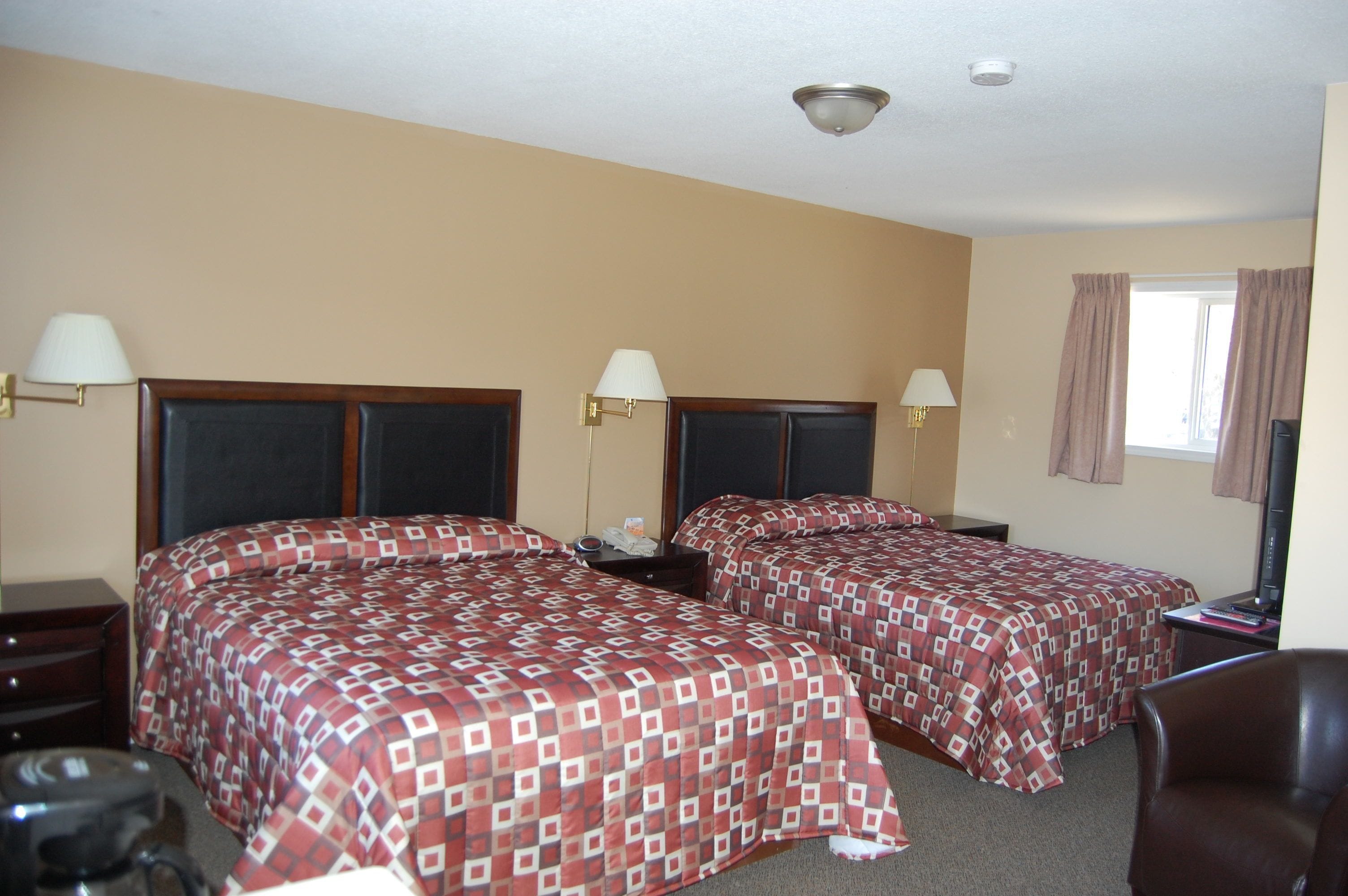 A hotel room with two beds, each with a headboard, bedside tables, lamps, and a window with curtains.