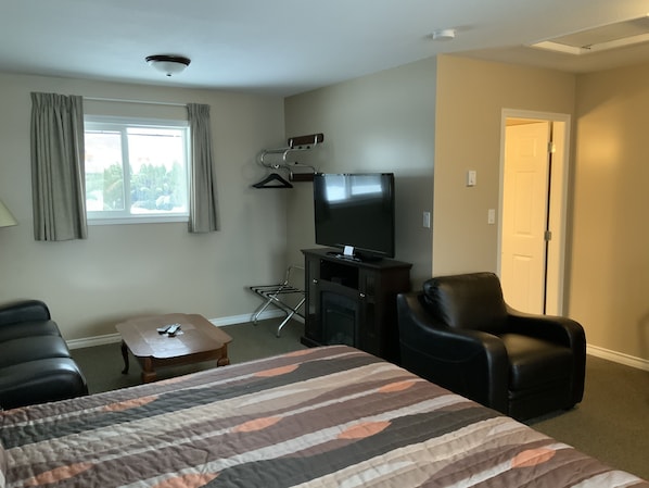 A hotel room with a bed, a TV, a desk, a chair, and a window with curtains.