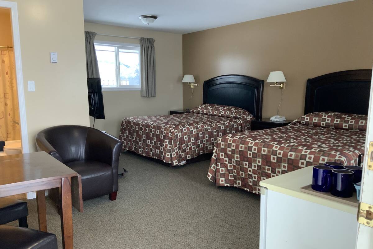 A hotel room with two beds, a desk, a chair, and a TV.