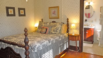 A bedroom with a four-poster bed, a nightstand with a lamp, and a bathroom visible through an open door.