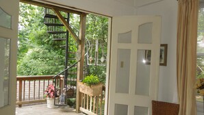 Une terrasse en bois avec un escalier menant à un balcon, une chaise en osier et une plante en pot.