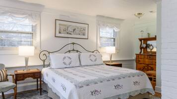 A bedroom with a bed, two bedside tables with lamps, a wooden dresser, a chair, and a framed picture on the wall.
