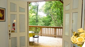 Une terrasse en bois avec une chaise et un tapis, une porte équipée d’un détecteur d’incendie, et une vue sur les arbres.