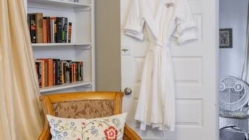 Una habitación con una silla de madera, una bata blanca colgada en la puerta y una estantería con libros.