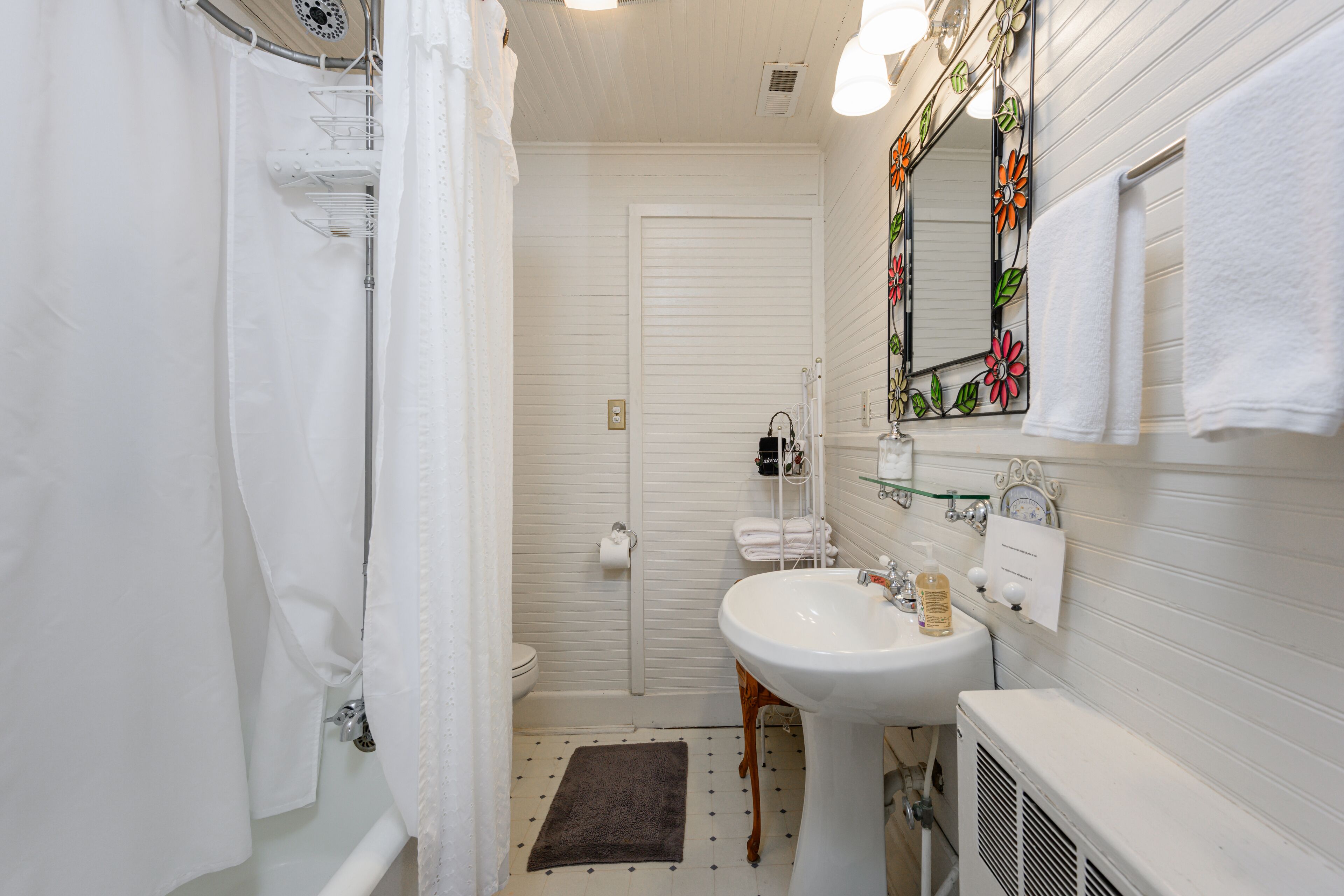 Casa de banho com lavatório branco, espelho com design floral e cortina de chuveiro.