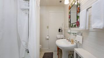 Casa de banho com lavatório branco, espelho com design floral e cortina de chuveiro.