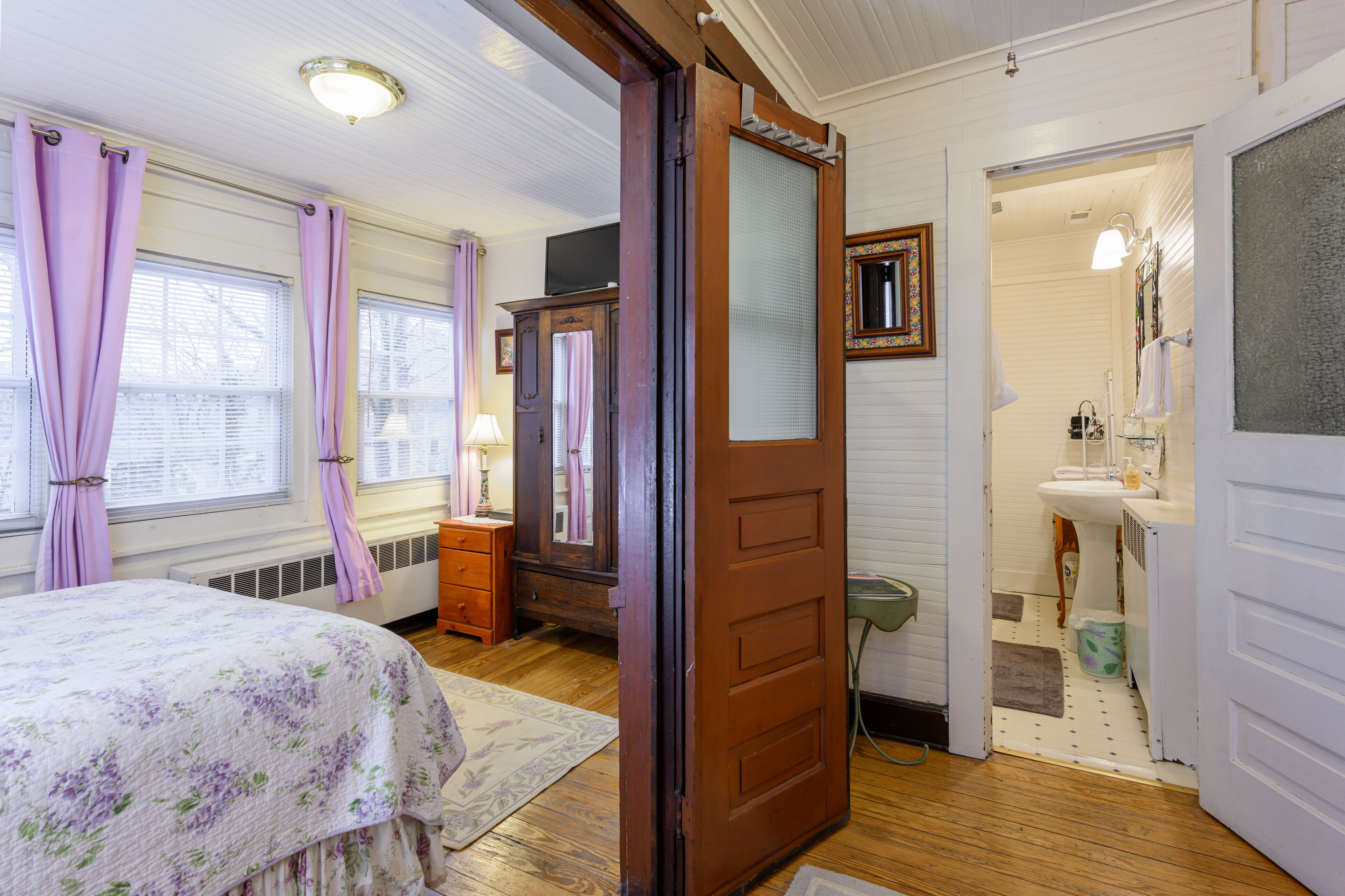 A bedroom with a bed, dresser, and a bathroom with a sink and mirror.