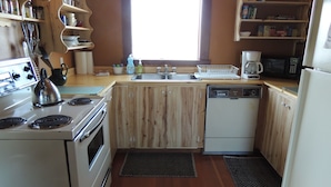 Una cocina compacta con armarios de madera, una estufa blanca, lavavajillas y una ventana que proporciona luz natural.