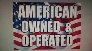 A sign with the text "AMERICAN OWNED & OPERATED" on a background featuring the American flag. - Classic Motel (Higginsville)