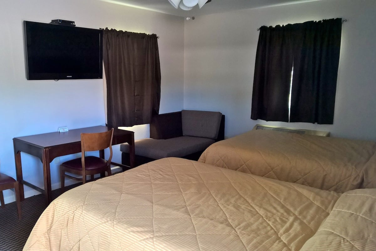 A hotel room with two beds, a desk, a chair, a television, and curtains.