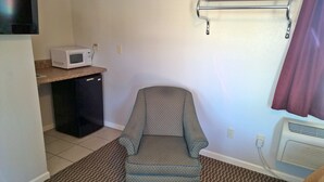 Une pièce compacte comprenant un coin cuisine, un petit réfrigérateur, un four à micro-ondes, une chaise à motifs, un radiateur et un rideau.