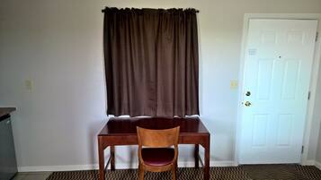 A room with a wooden desk and chair, a brown curtain, a white door, and a patterned rug.