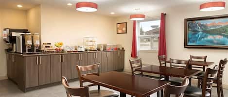 A dining area with a wooden table and chairs, a kitchen with a coffee machine, and a painting on the wall.