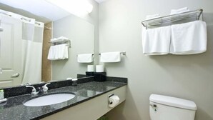 A bathroom with a sink, mirror, towel rack, toilet, and trash can. - Travelodge by Wyndham Kindersley (Kindersley)