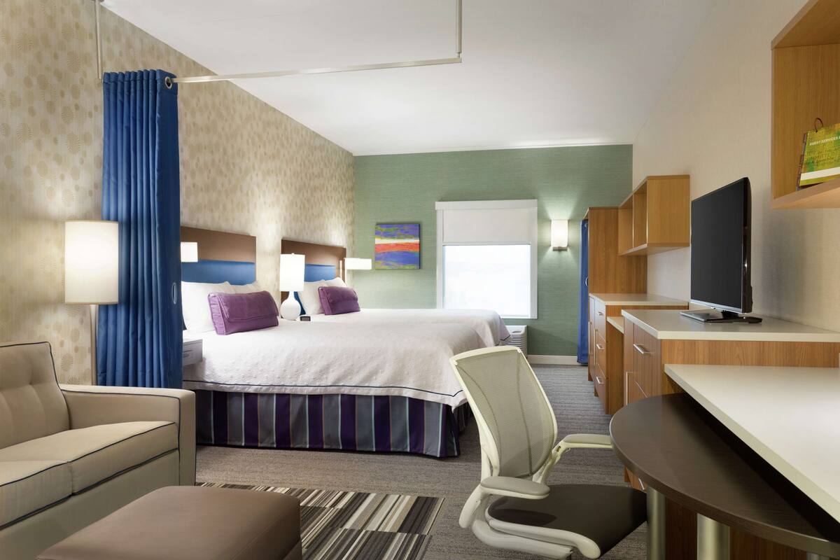 A hotel room with a bed, a desk, a chair, a sofa, and a television.