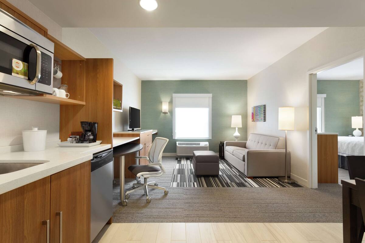 A modern hotel room with a kitchenette, a dining area, and a living space.