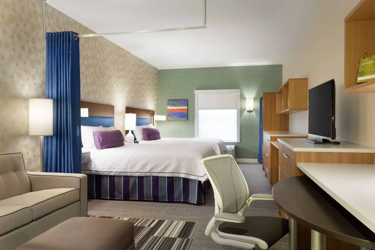 A hotel room with a bed, a desk, a chair, a sofa, and a TV.