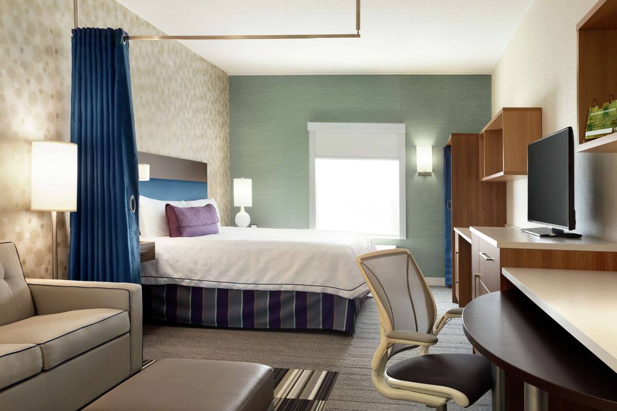 A hotel room with a bed, a desk, a chair, a TV, and a window.
