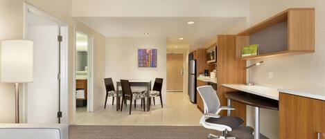 A modern hotel room with a dining area, kitchenette, and a large window.