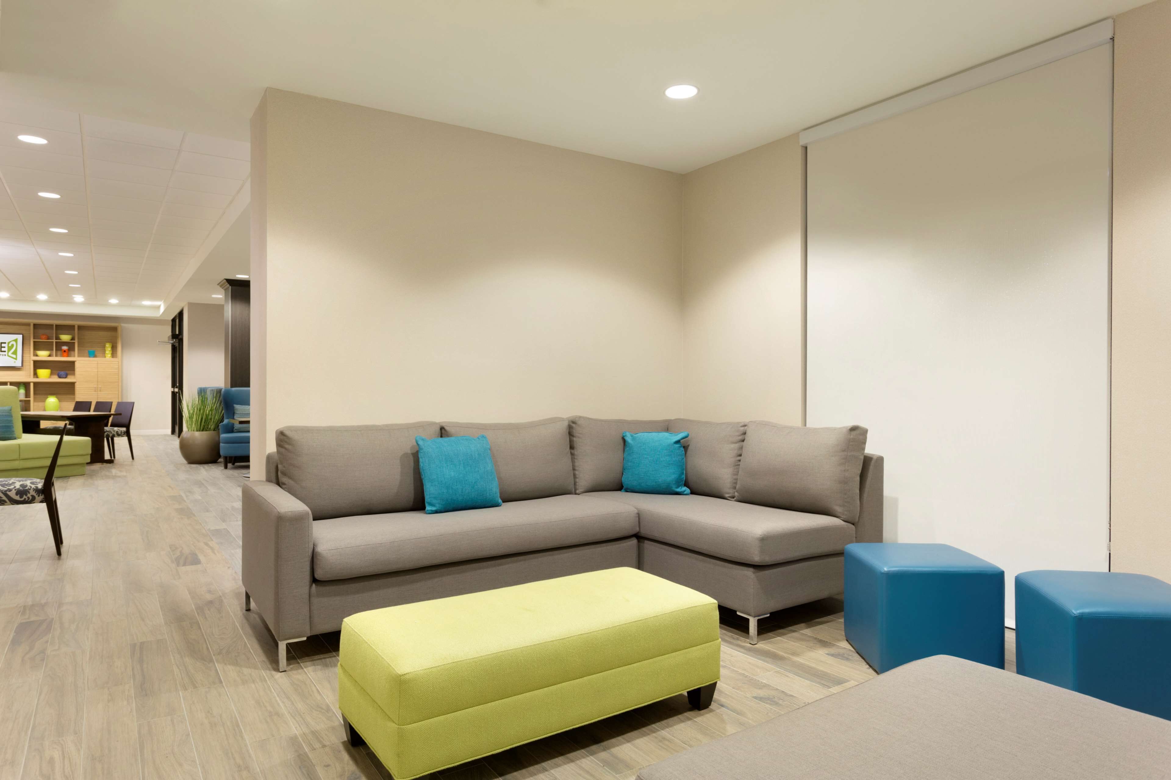 Een moderne woonkamer met een grijze hoekbank, een geel poufje en blauwe kussens.