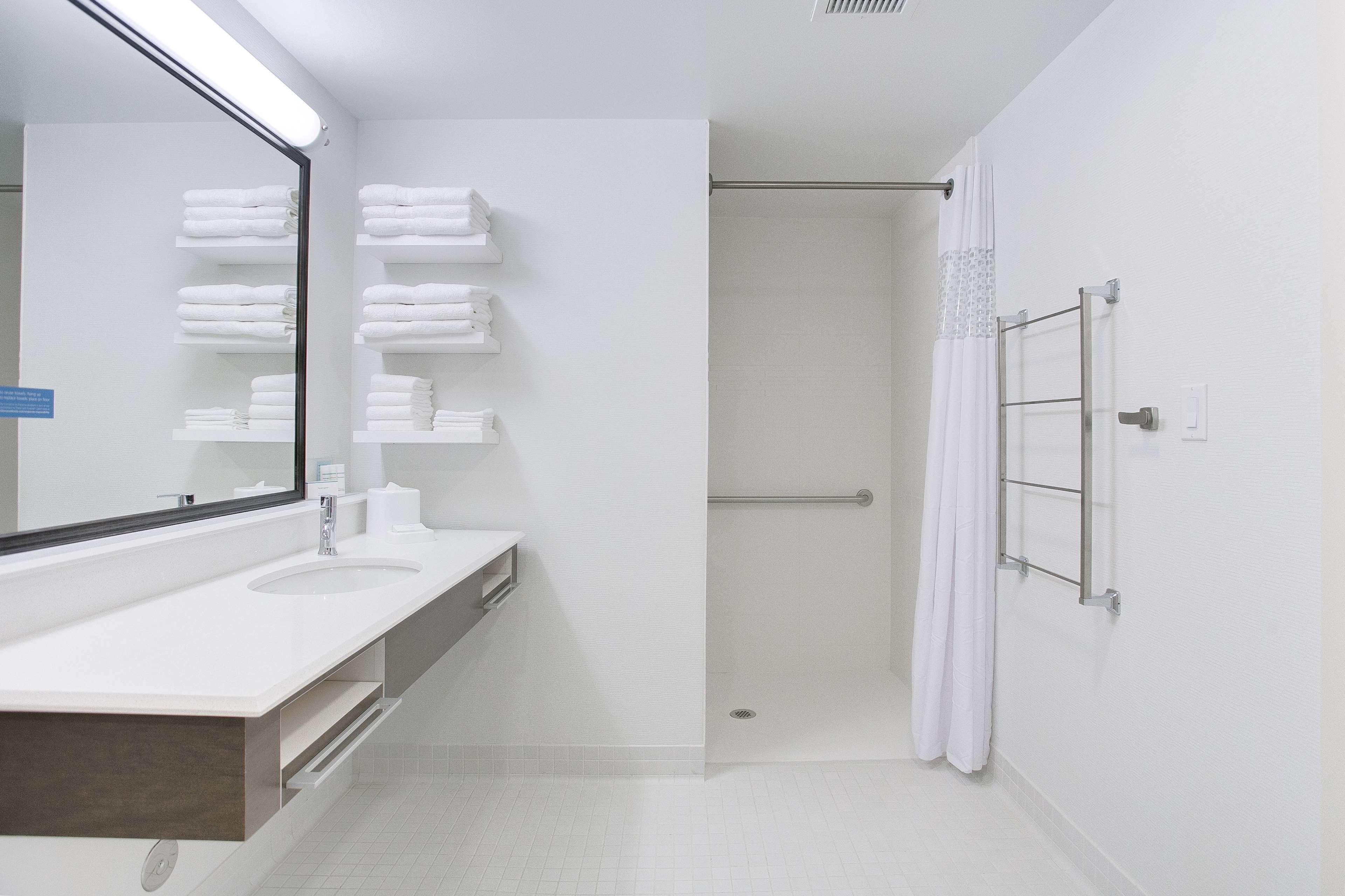 Un baño moderno con un espejo grande, dos lavamanos, una ducha con puerta de cristal y toallas ordenadas en estantes.