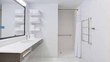 Un baño moderno con un espejo grande, dos lavamanos, una ducha con puerta de cristal y toallas ordenadas en estantes.