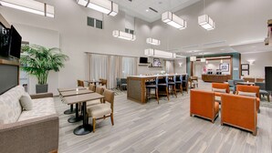 Un lobby de hotel amplio con diseño moderno, que cuenta con una zona de estar grande con sofás y mesas, un mostrador de recepción y una planta en maceta de gran tamaño.