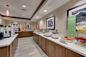 A breakfast buffet area with a variety of food options, including fruits and beverages, and a coffee station.