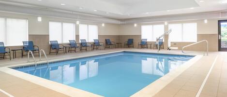 A swimming pool with blue tiles, surrounded by blue chairs and a tiled floor.