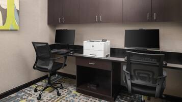 A modern office space with two desks, each with a computer and printer, and office chairs.