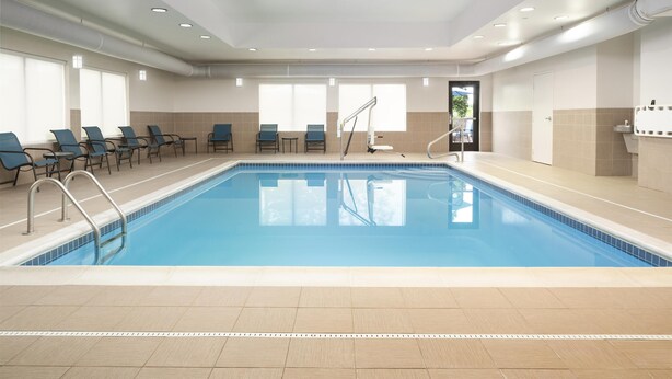 A swimming pool with blue tiles, surrounded by lounge chairs and a tiled floor. - Hampton Inn Fairmont (Fairmont)