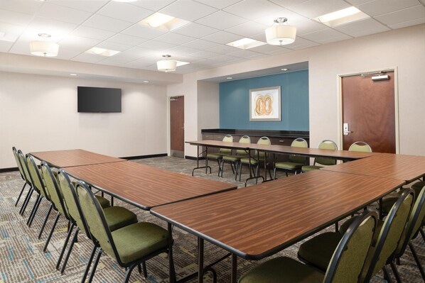 Une salle de conférence avec une longue table, des chaises vertes, un téléviseur à écran plat et un mur d’accent bleu.