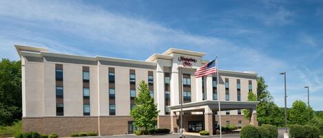 Een Hampton Inn hotel met een moderne gevel, een vlag en een parkeerplaats.