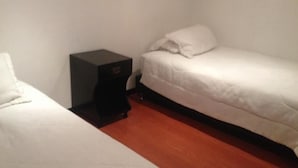 A small, single-room with two beds, a nightstand, and a wooden floor. - Hotel Casa La Embajada Colonial (Bogotá)