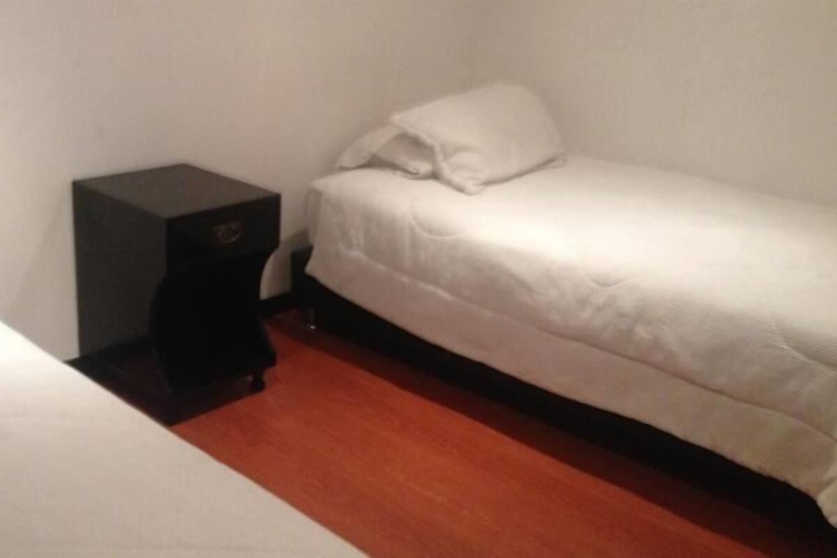 A small, single-room with two beds, a nightstand, and a wooden floor.