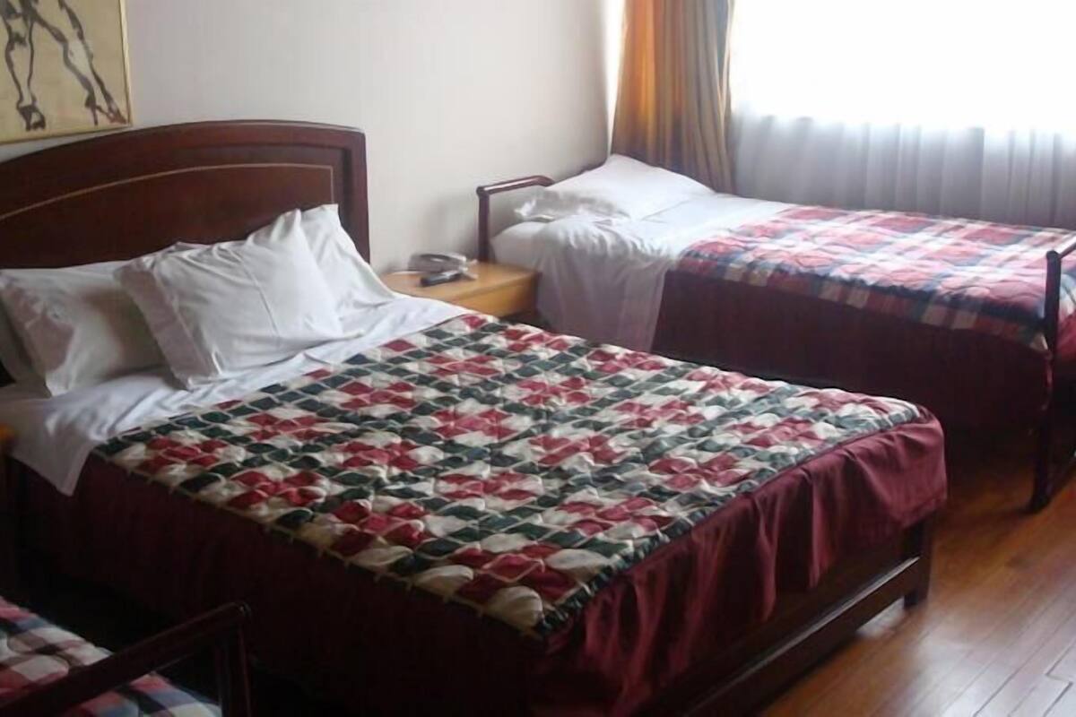 A hotel room with two single beds, a wooden headboard, a nightstand, and a bedside table.
