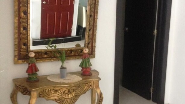 A hallway with a mirror, a red door, and a small table with decorative items. - Hotel Casa La Embajada Colonial (Bogotá)