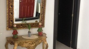 A hallway with a mirror, a red door, and a small table with decorative items. - Hotel Casa La Embajada Colonial (Bogotá)